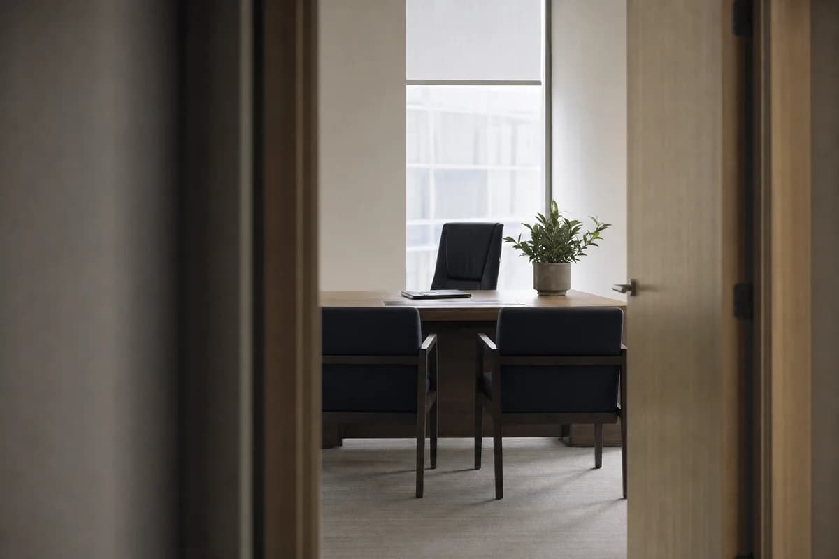 A quiet single-occupancy office with a desk and two visitor chairs, seen from the corridor
