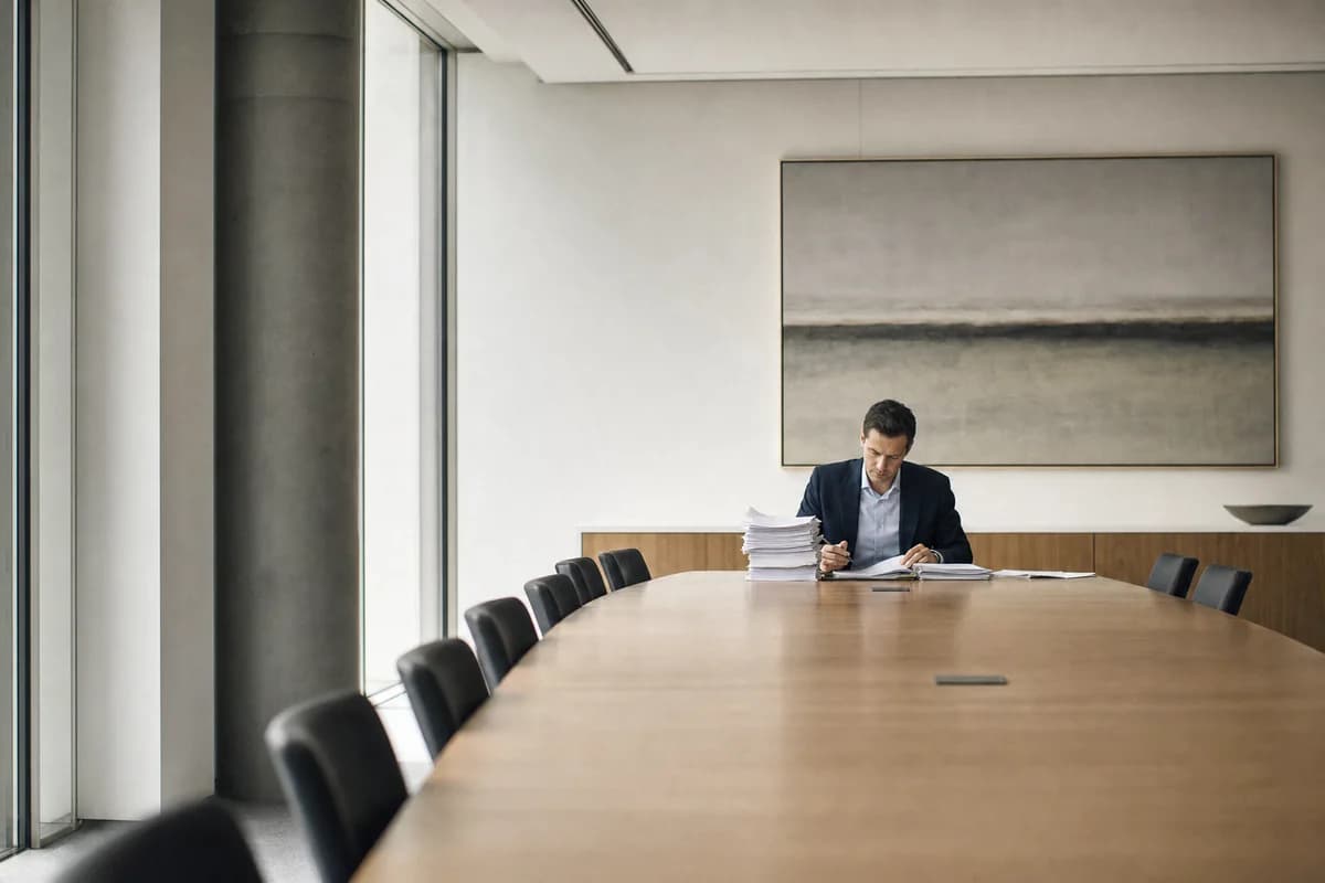One person working alone through a stack of printed evidence at an otherwise empty boardroom table