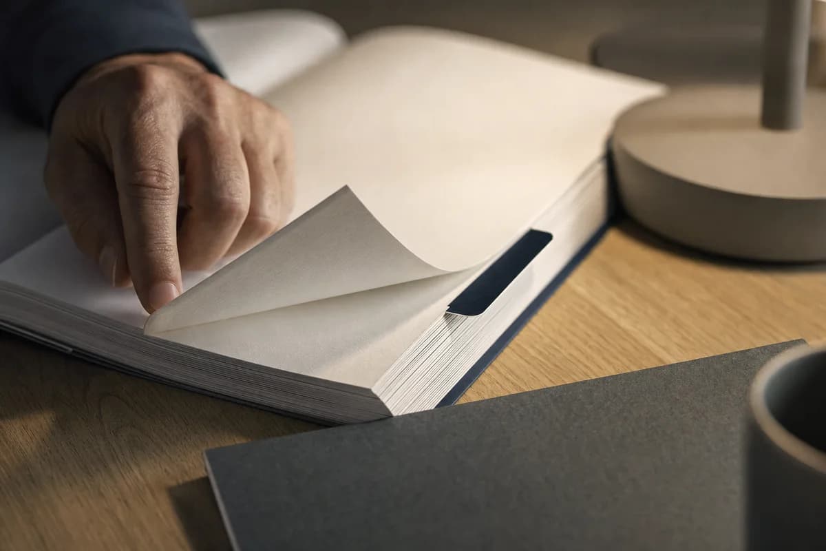 A thick printed audit report open flat at a tabbed section divider, a hand turning a page
