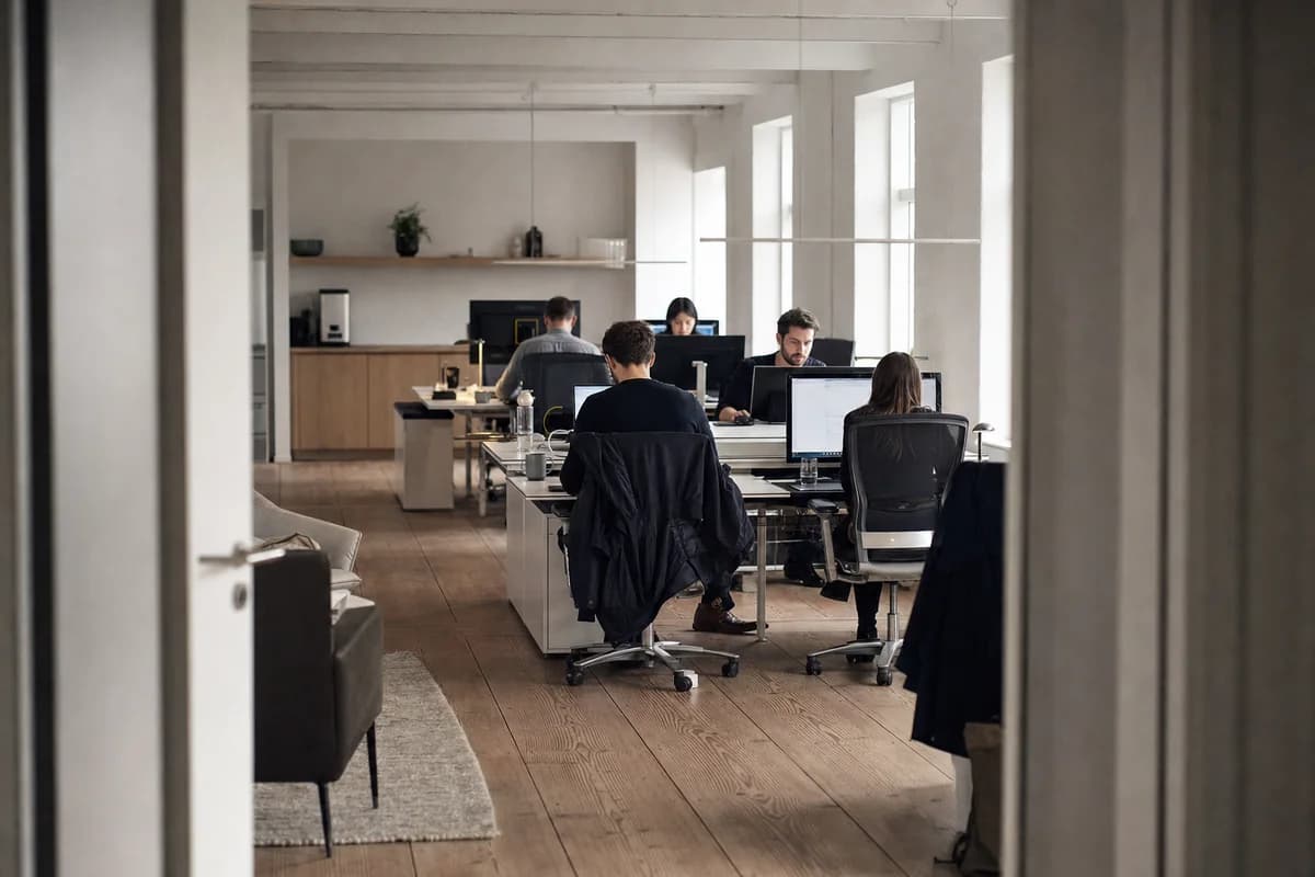 A small growing company office with seven desks and five people working