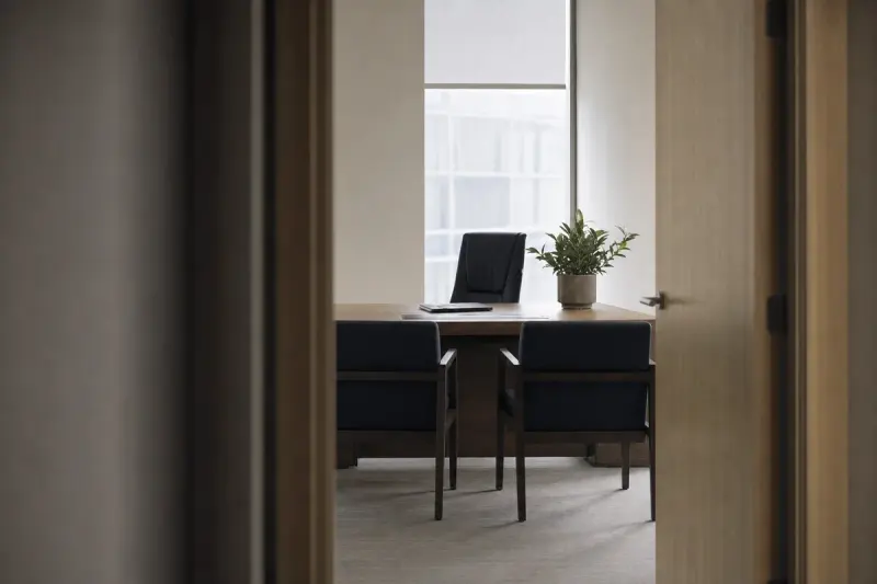 A quiet single-occupancy office with a desk and two visitor chairs, seen from the corridor